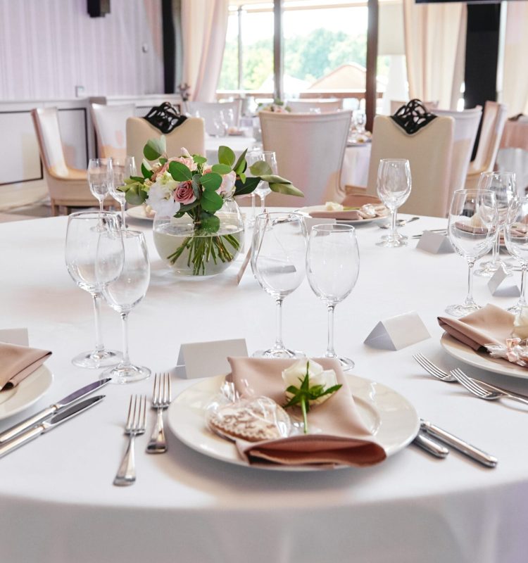 Table setting with blank guest card, white plate with beige serviette, rose, heart and cutlery on table, copy space. Place setting at wedding reception. Table served for wedding banquet in restaurant