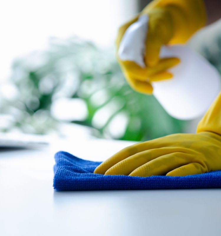 Person cleaning the room, cleaning staff is using cloth and spraying disinfectant to wipe the tables in the company office room. Cleaning staff. Maintaining cleanliness in the organization.